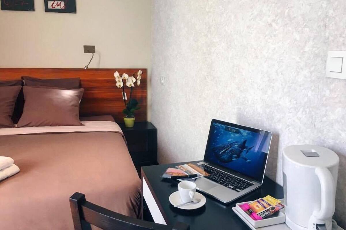 A hotel room with a bed, a laptop on a desk, a coffee maker, and a small table with a cup and some items.