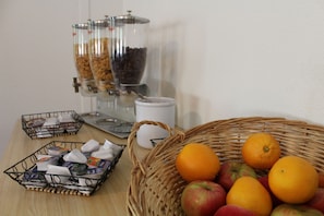A breakfast setup with a coffee dispenser, a basket of fruits, and a tray of pastries. - CIST Domaine d'Ariane (Mondonville)