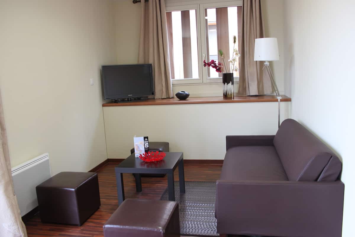 A living room with a sofa, a television, a small table with a vase, and a lamp.