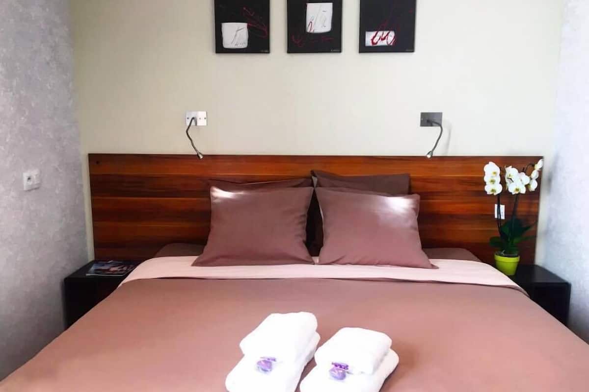 A neatly made bed with two pillows, a bedside table with a lamp, and three framed artworks on the wall.