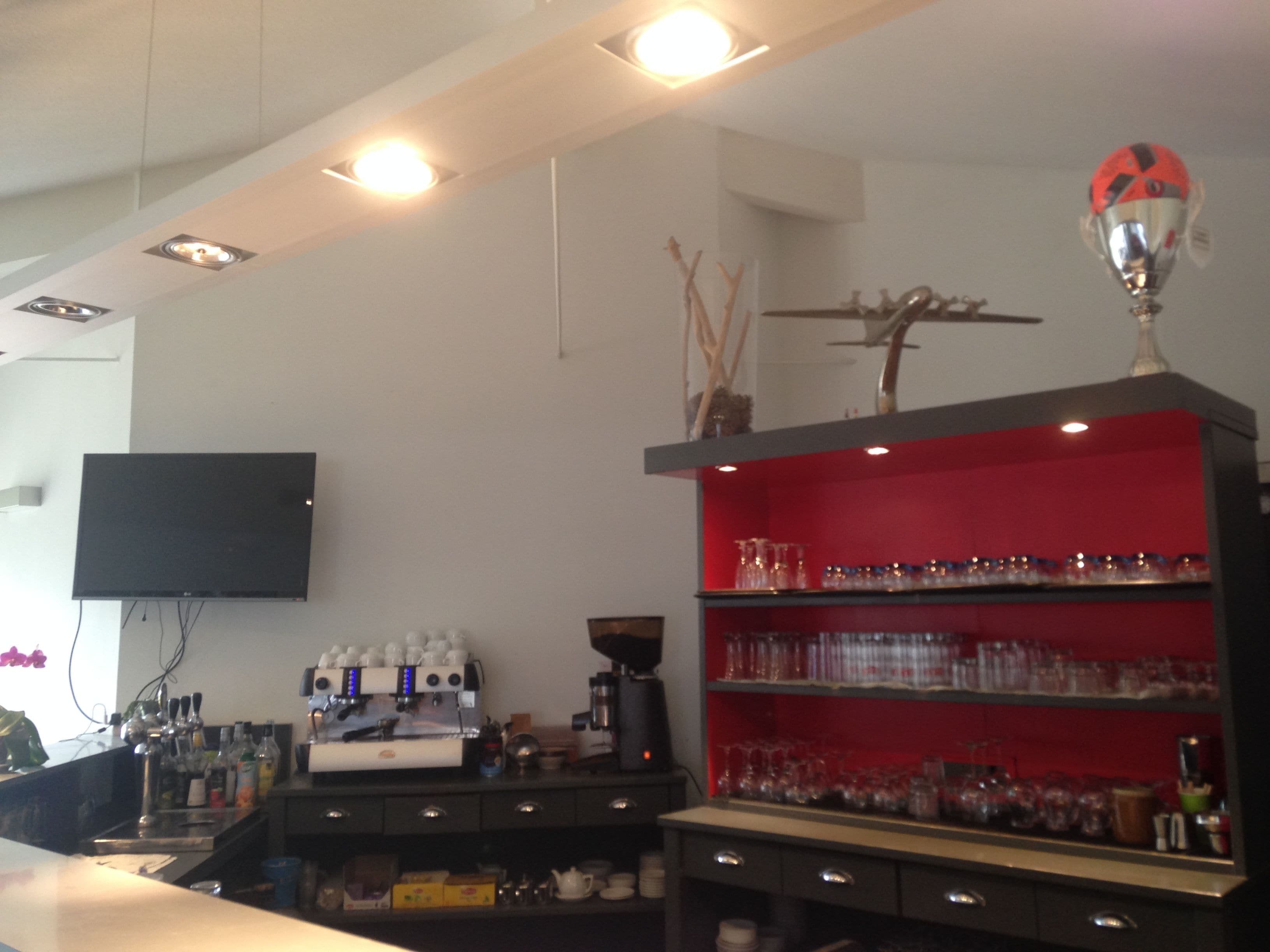 A bar area with a flat-screen TV, espresso machine, and shelves with glasses and bottles.