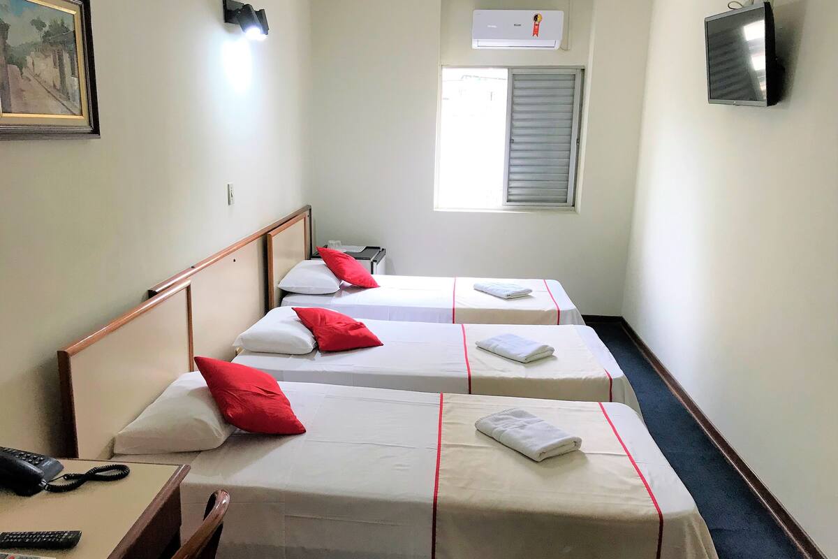 Une chambre d’hôtel avec deux lits simples, chacun agrémenté d’un oreiller rouge et blanc, une table de chevet avec un téléphone et un téléviseur fixé au mur.