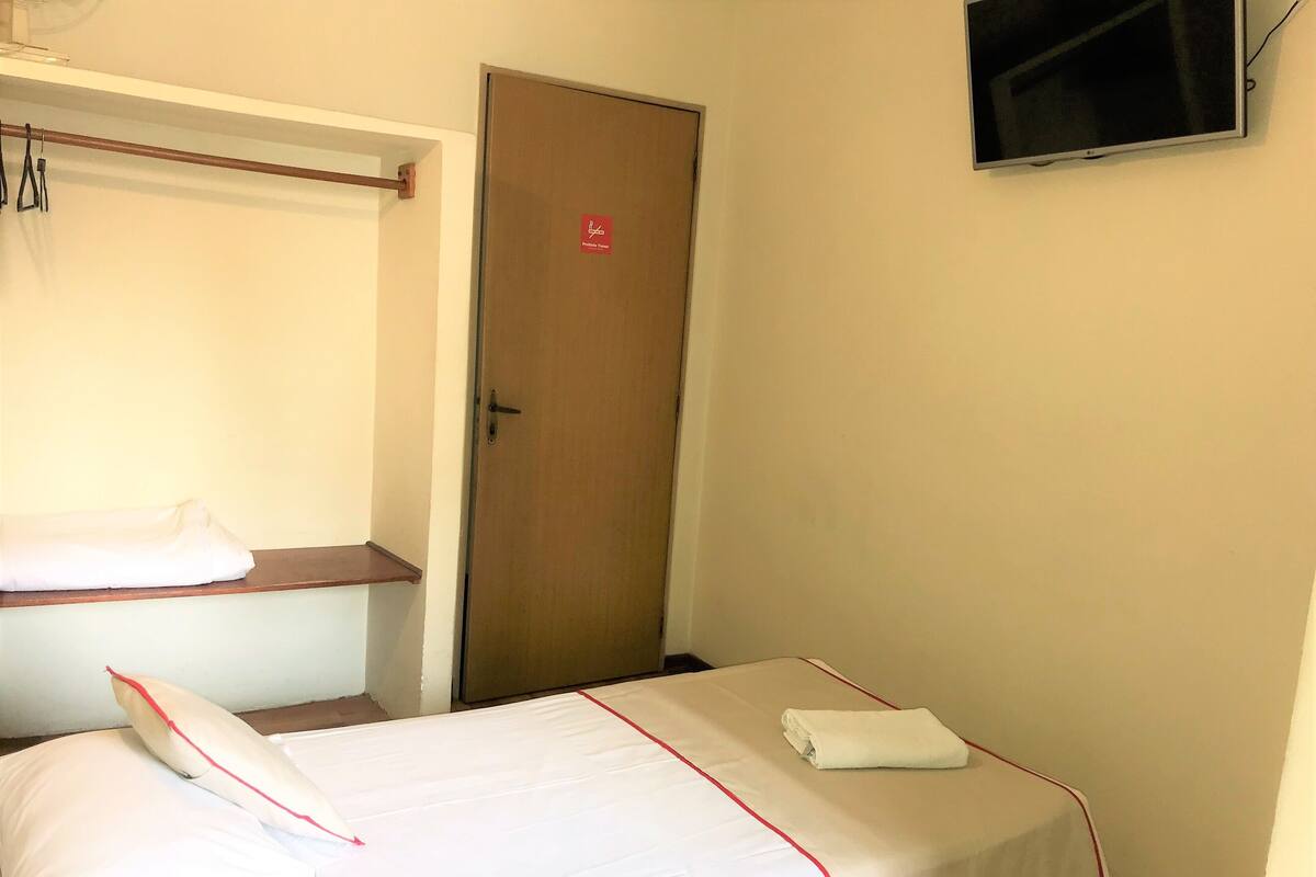 Une chambre d’hôtel avec un lit, un téléviseur fixé au mur et une porte.
