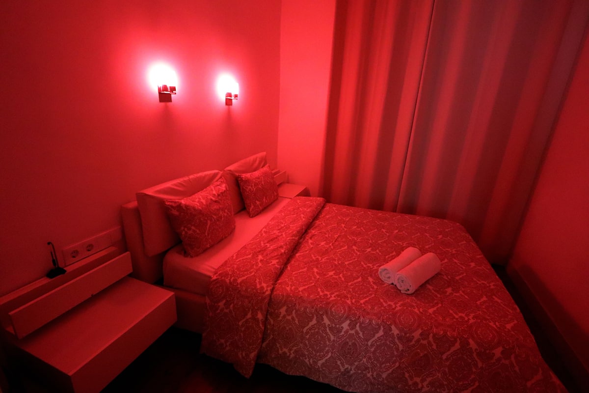 Una habitación con cama, mesita de noche y dos lámparas de pared.