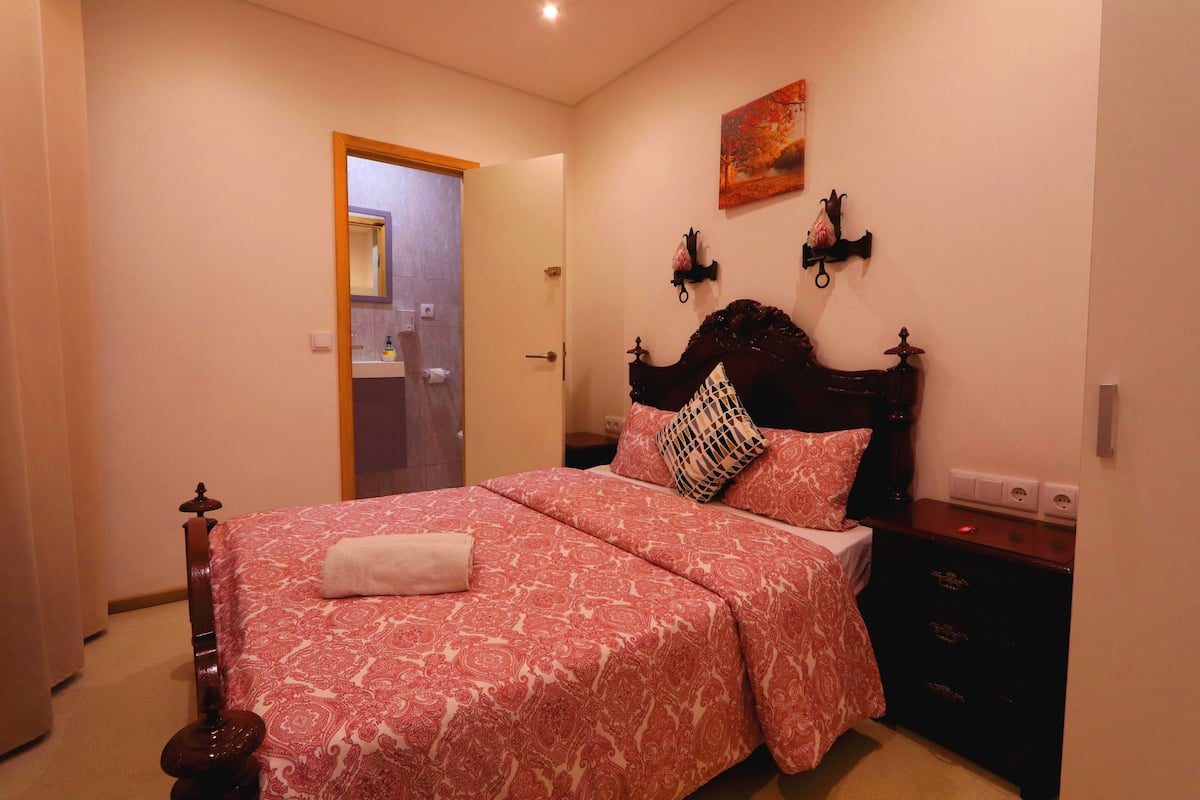 Un dormitorio con cama, mesita de noche, lámpara de pared y puerta que da a otra habitación.