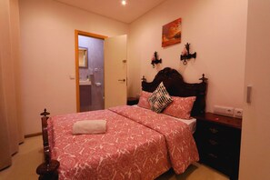 Ein Schlafzimmer mit einem Bett, einem Nachttisch, einer Wandleuchte und einer Tür zu einem anderen Raum.
