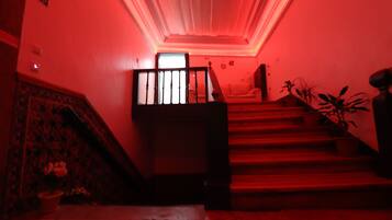 A staircase with a red-lit ceiling, a wooden handrail, and a potted plant on the right.