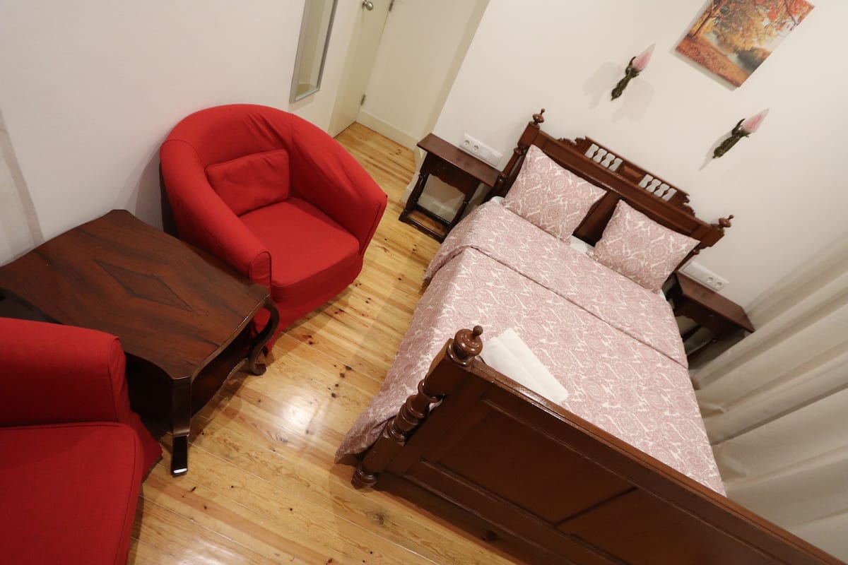 Un dormitorio con una cama de madera, un sillón rojo y una mesita de noche de madera.