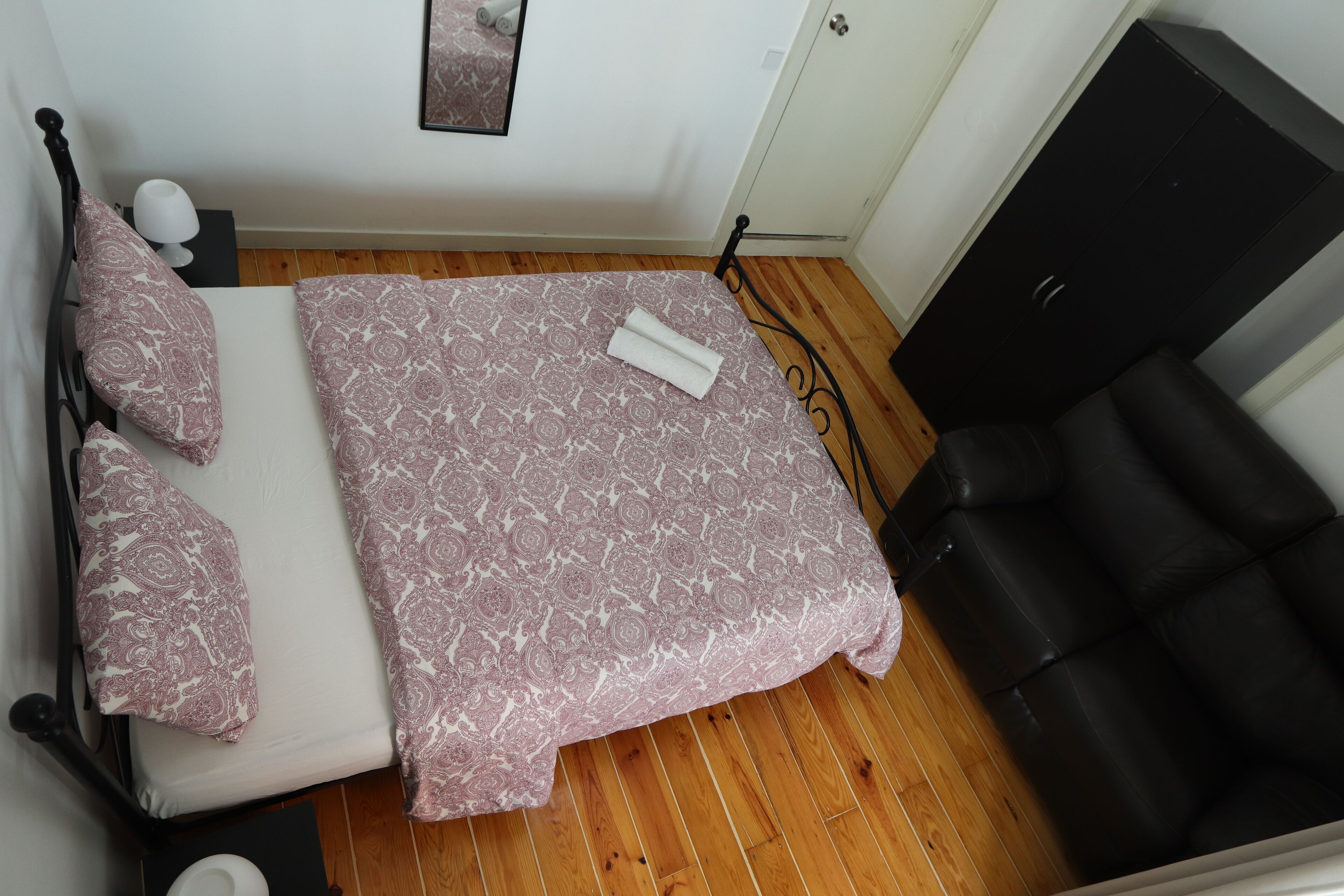 A bedroom with a bed, a black leather sofa, a wooden floor, and a white door.
