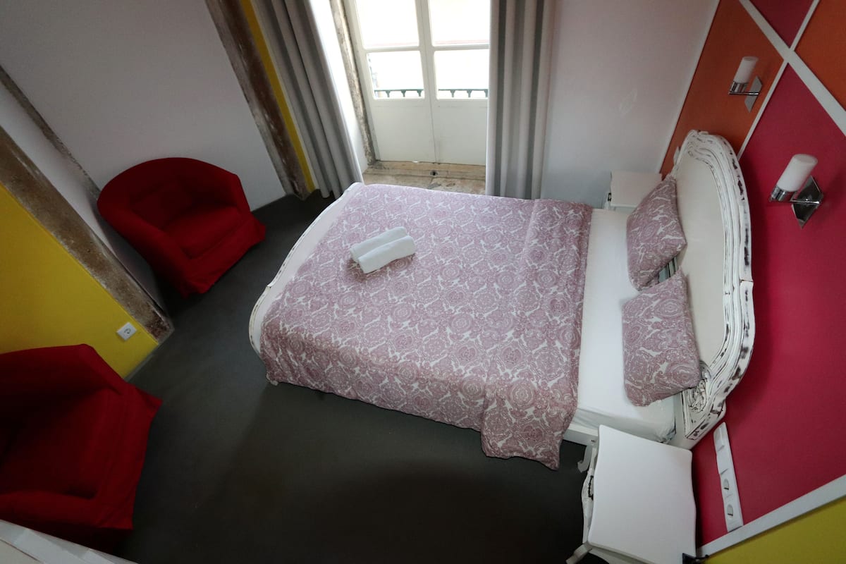 Un dormitorio con una cama, una silla roja y una ventana con cortinas.