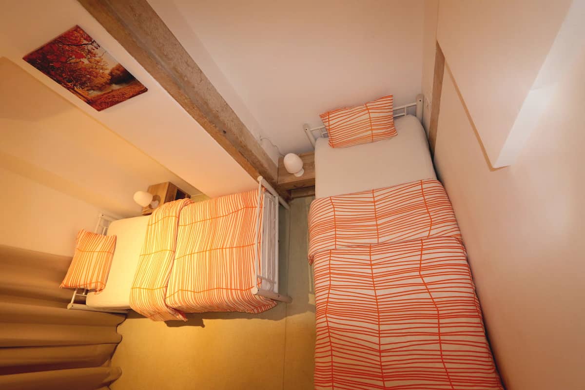 Un dormitorio con dos camas, cada una con ropa de cama a rayas, un radiador y un cuadro en la pared.