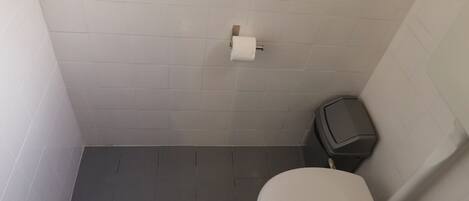 A small bathroom with a white toilet, a trash bin, and a toilet paper holder on the wall.