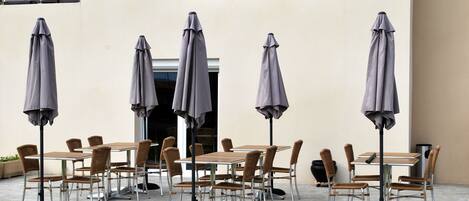 Outdoor seating with tables and chairs, umbrellas, and a building facade.