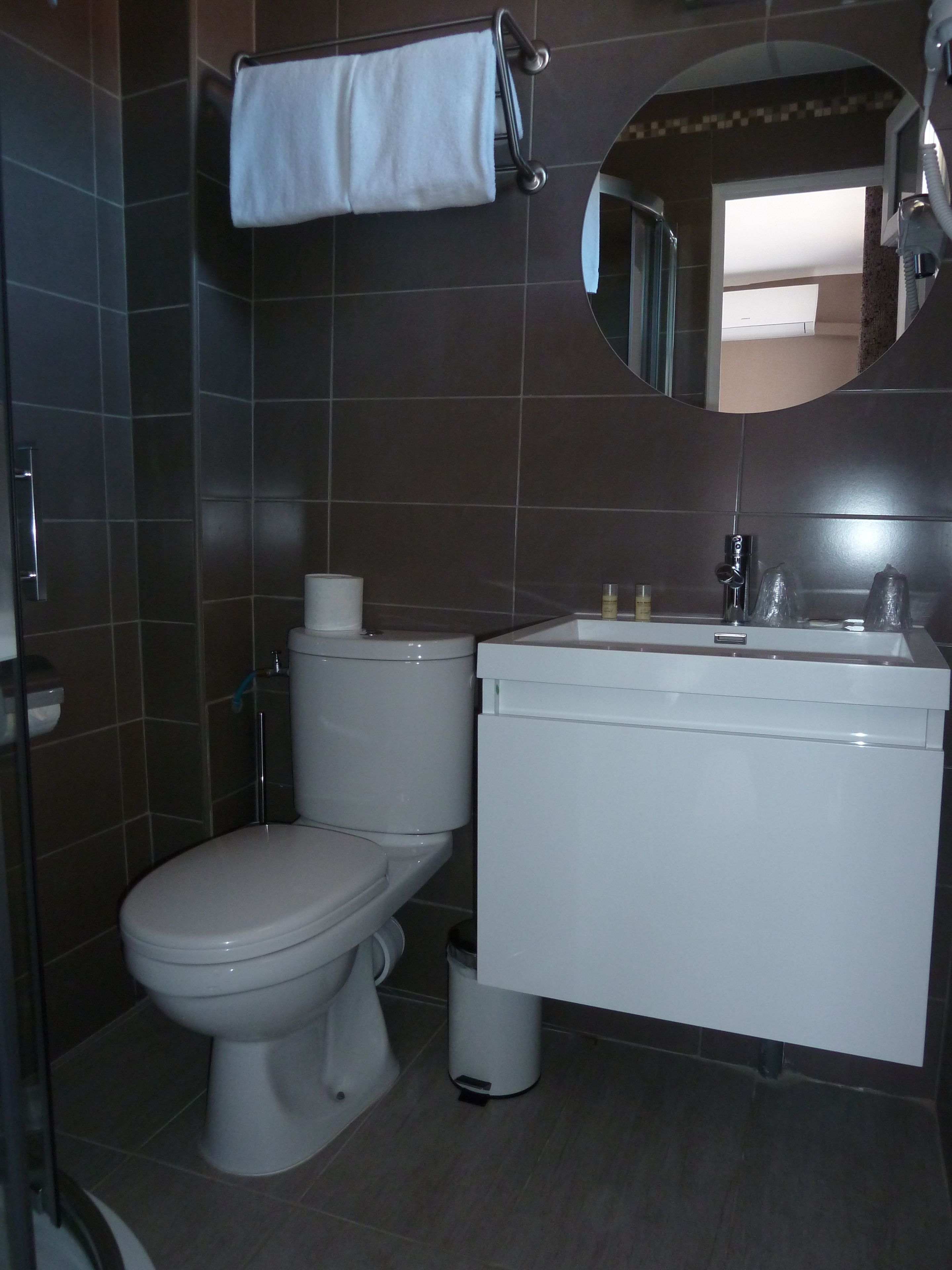 A bathroom with a toilet, sink, mirror, and towel rack.
