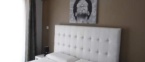 A bedroom with a large bed, a headboard, a wall-mounted air conditioner, and a painting.