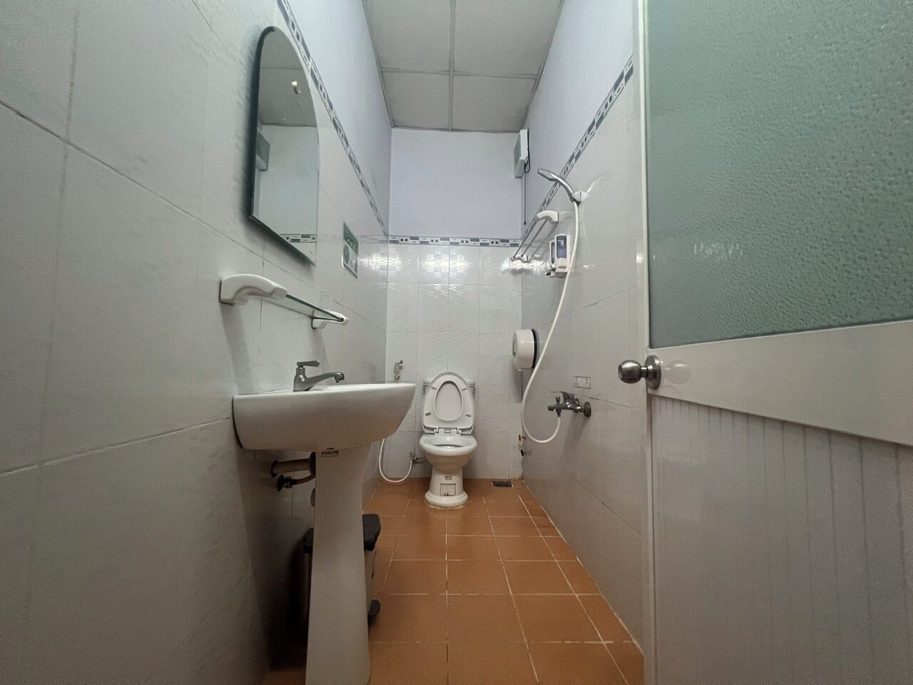 A small, narrow bathroom with a white sink, a toilet, and a shower.