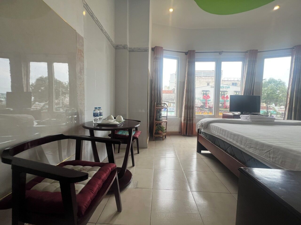 A hotel room with a bed, a TV, a dining table with chairs, and a view of the outside.