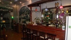 Zona de bar con mostrador de ladrillo y taburetes, un mural en la pared y estantes con botellas.