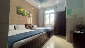 Habitación de hotel con dos camas, ventilador de techo, ventana con cortinas, un armario de madera y un cuadro en la pared.