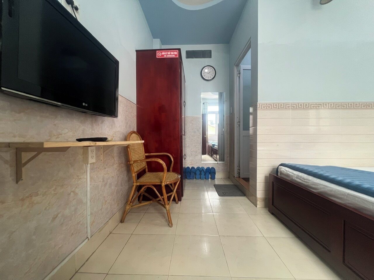 A hotel room with a bed, a TV mounted on the wall, a wooden chair, and a red door.