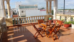 Un balcón con una mesa y sillas, plantas en macetas y vistas a edificios al fondo.