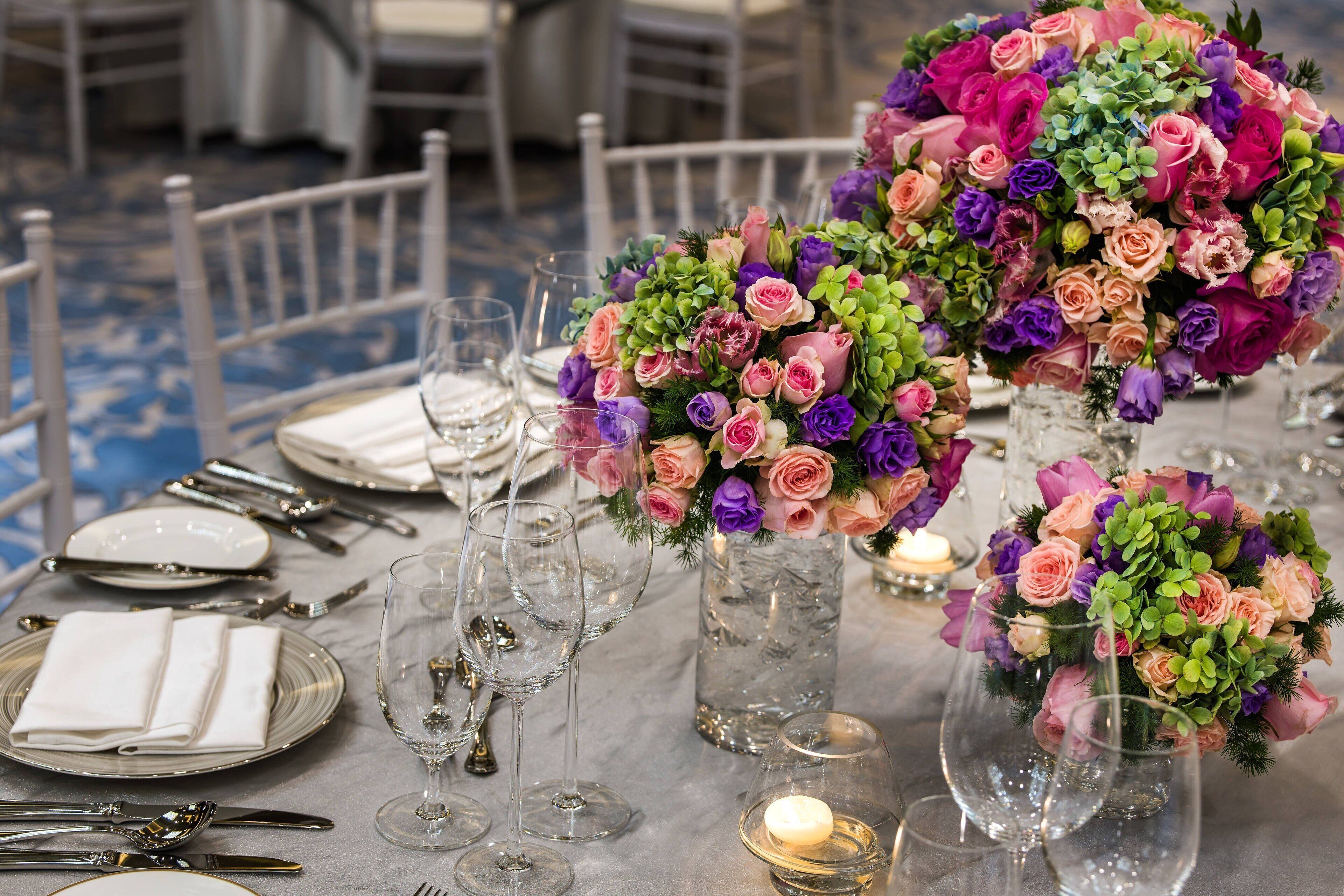 A table set for a formal event with clear glassware, folded napkins, and floral centerpieces.