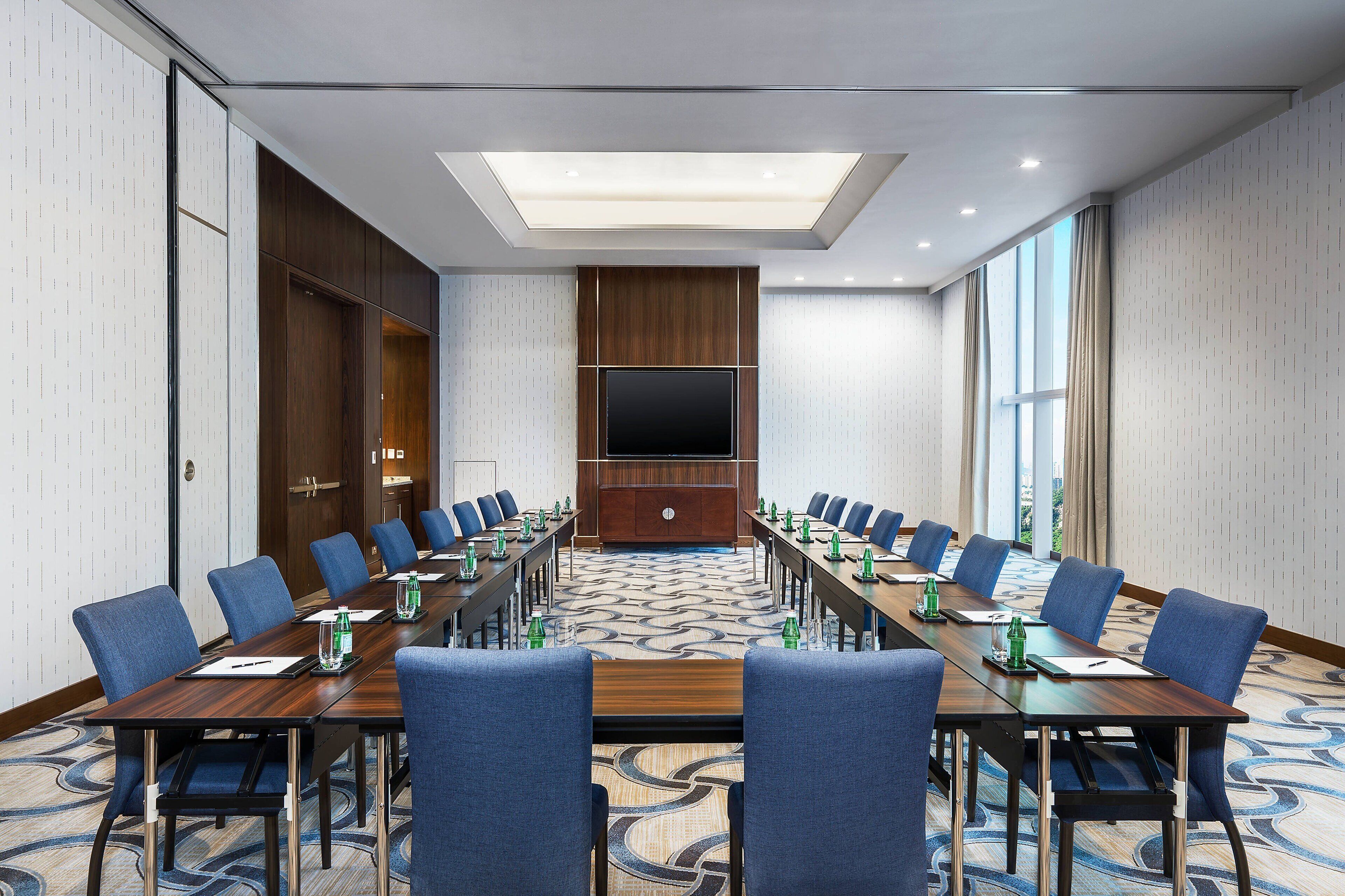 A conference room with a long table, blue chairs, and a flat-screen TV.