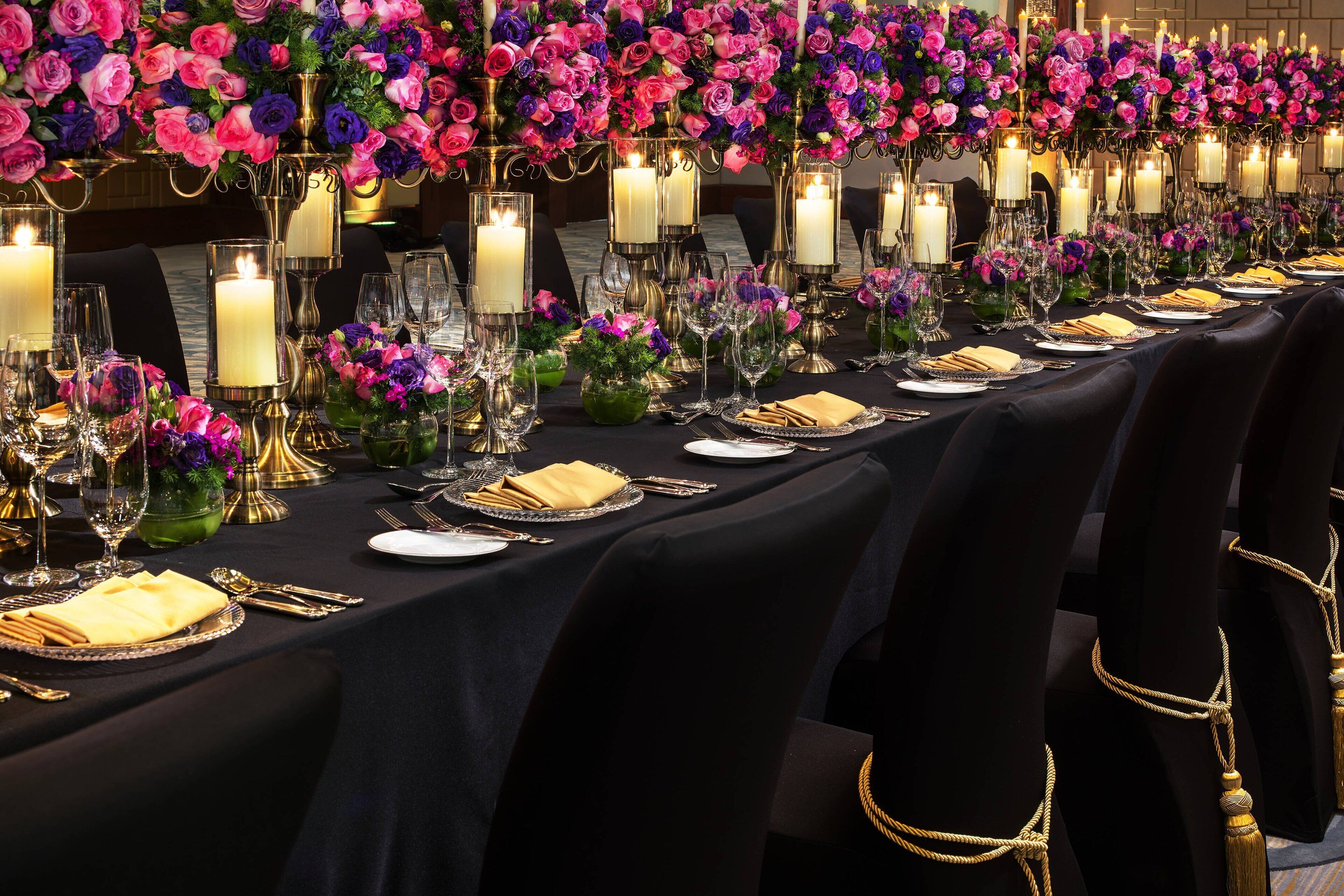A long dining table set with candles, glassware, and folded napkins, surrounded by chairs with gold accents.