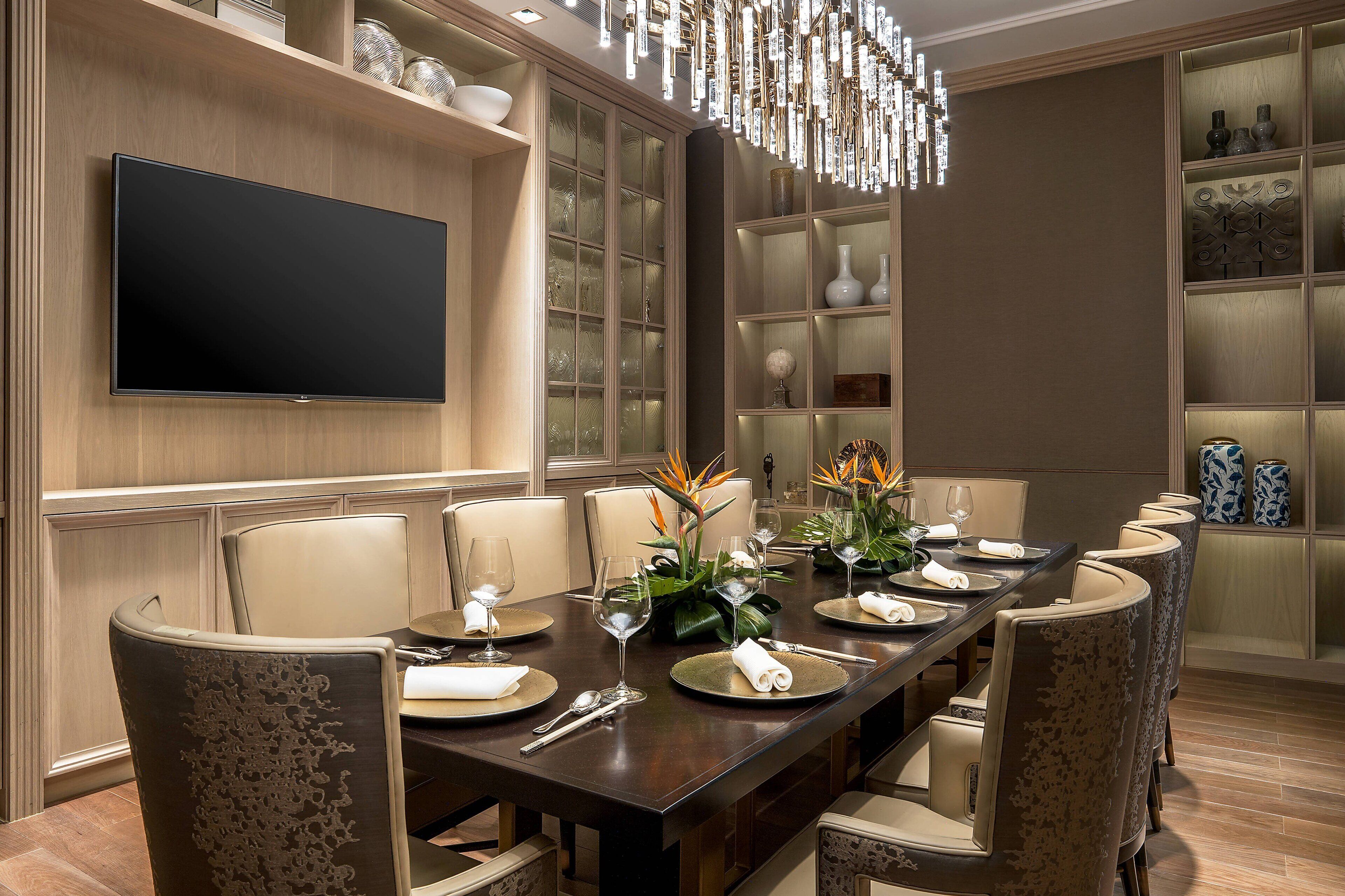 Un comedor con una mesa larga, sillas y un televisor de pantalla plana montado en la pared.
