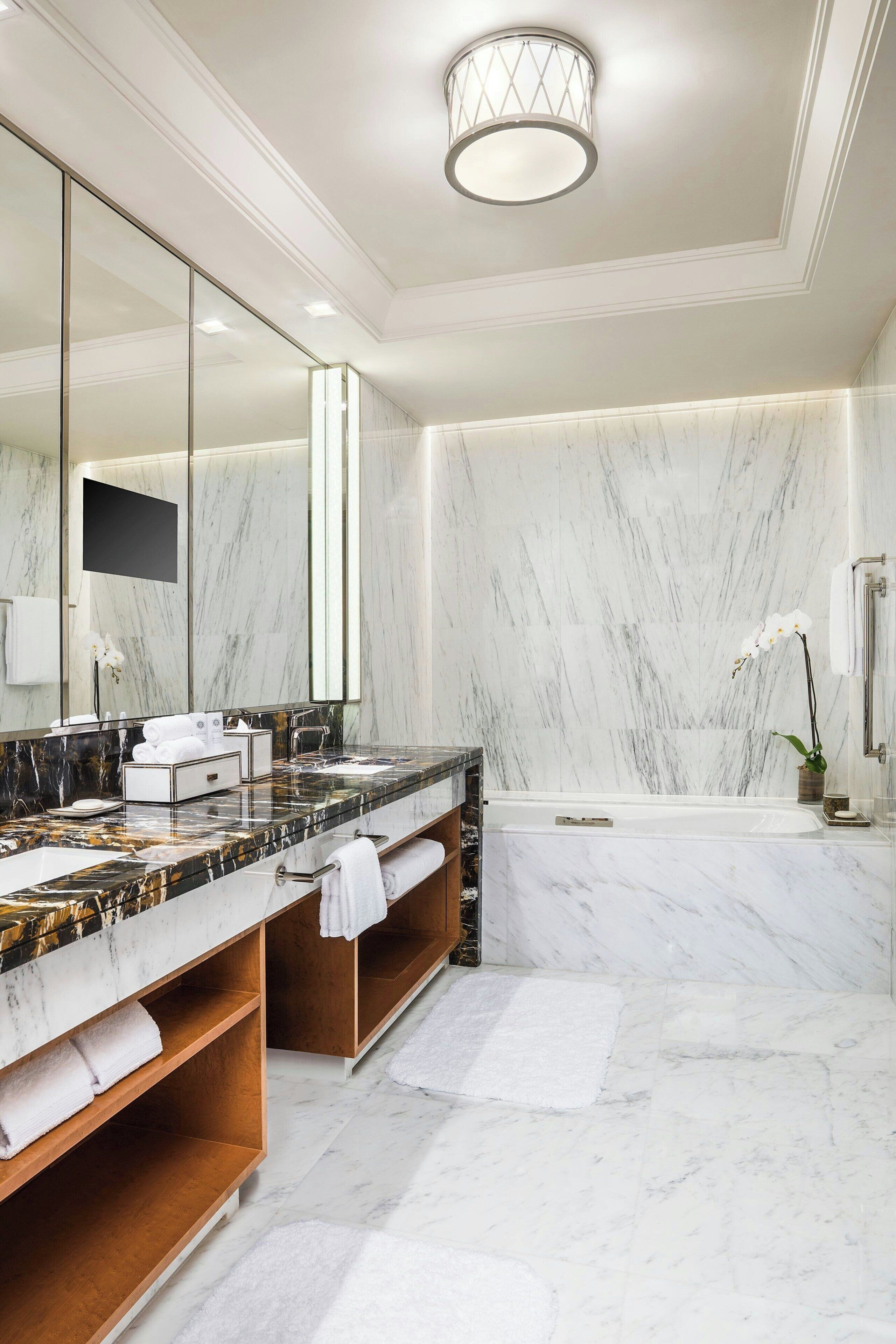 A modern bathroom with marble walls, a large mirror, a bathtub, and a vanity with a marble countertop.