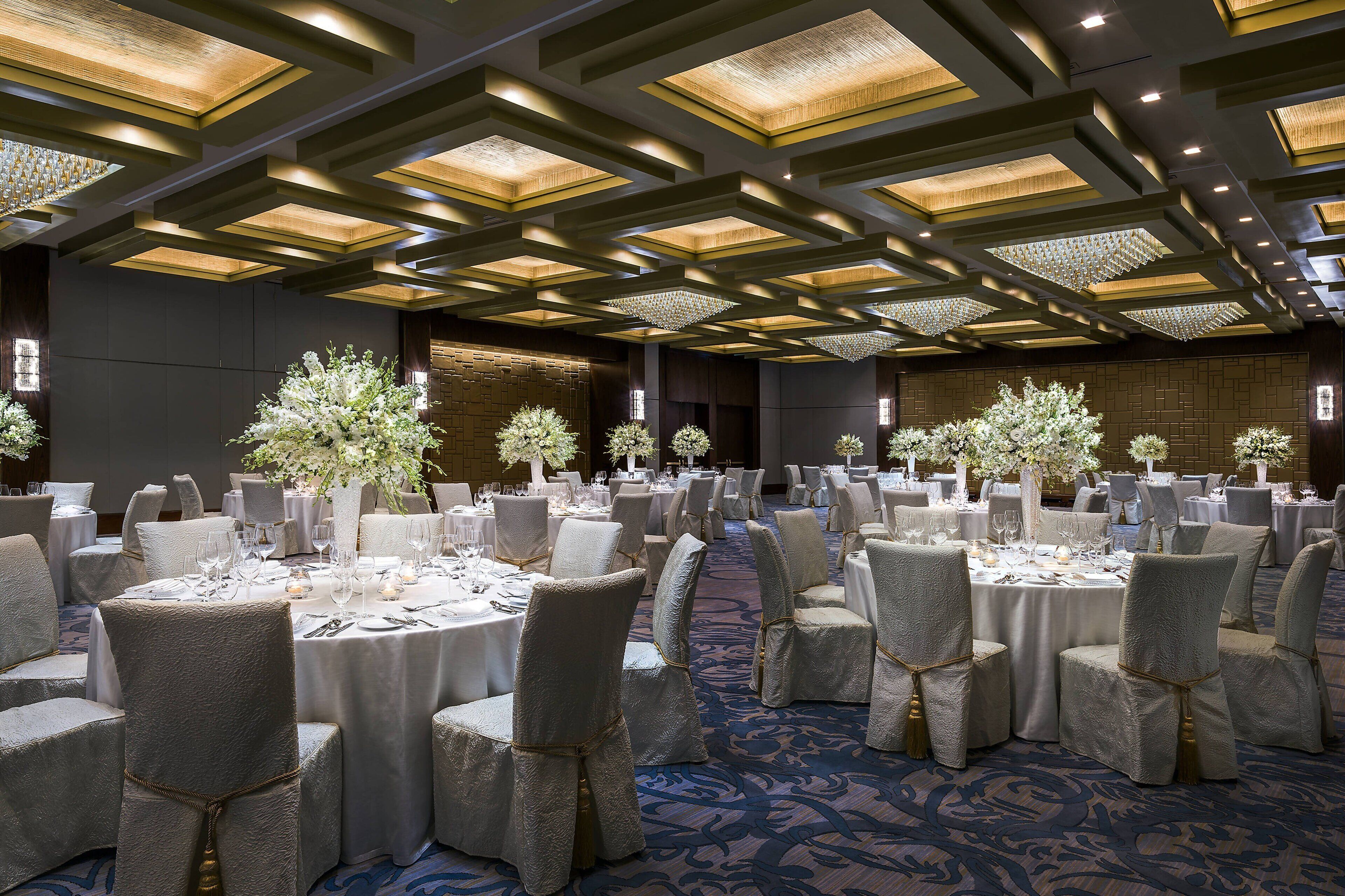 A banquet hall with round tables, chairs, and floral centerpieces.
