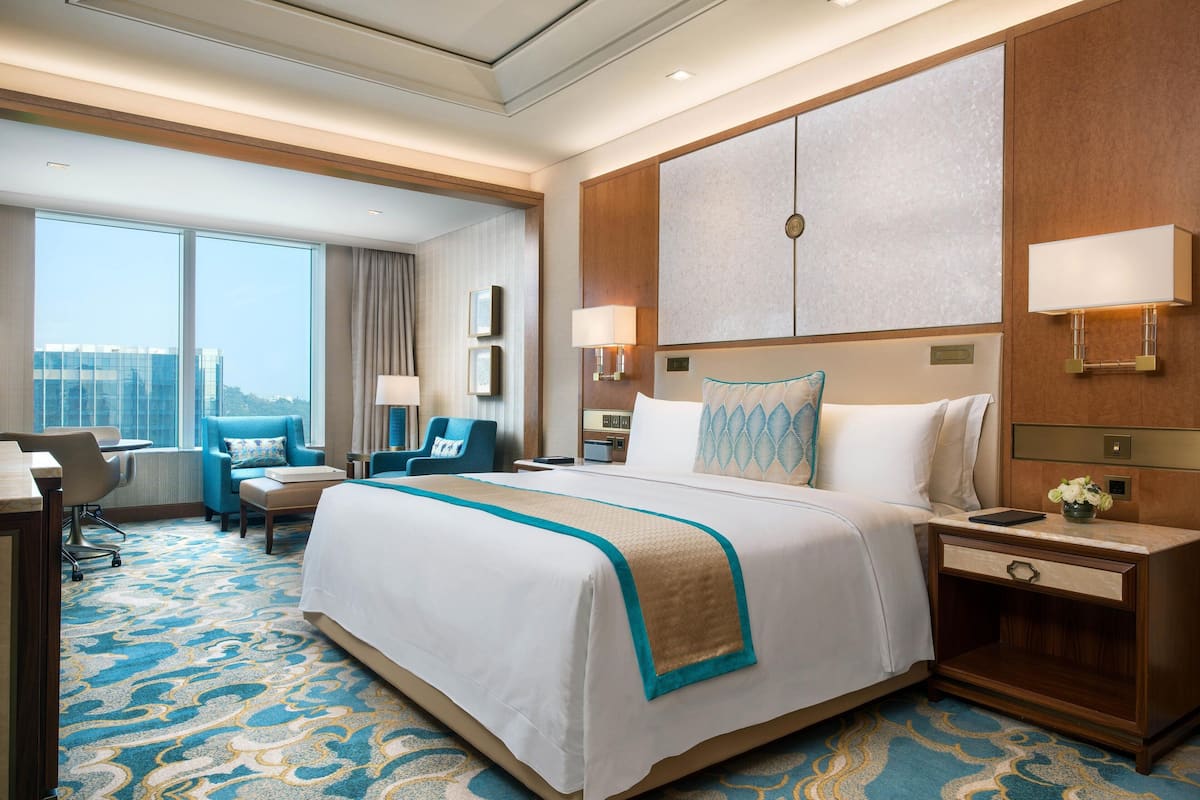 A hotel room with a large bed, a desk, a chair, and a view of the city.