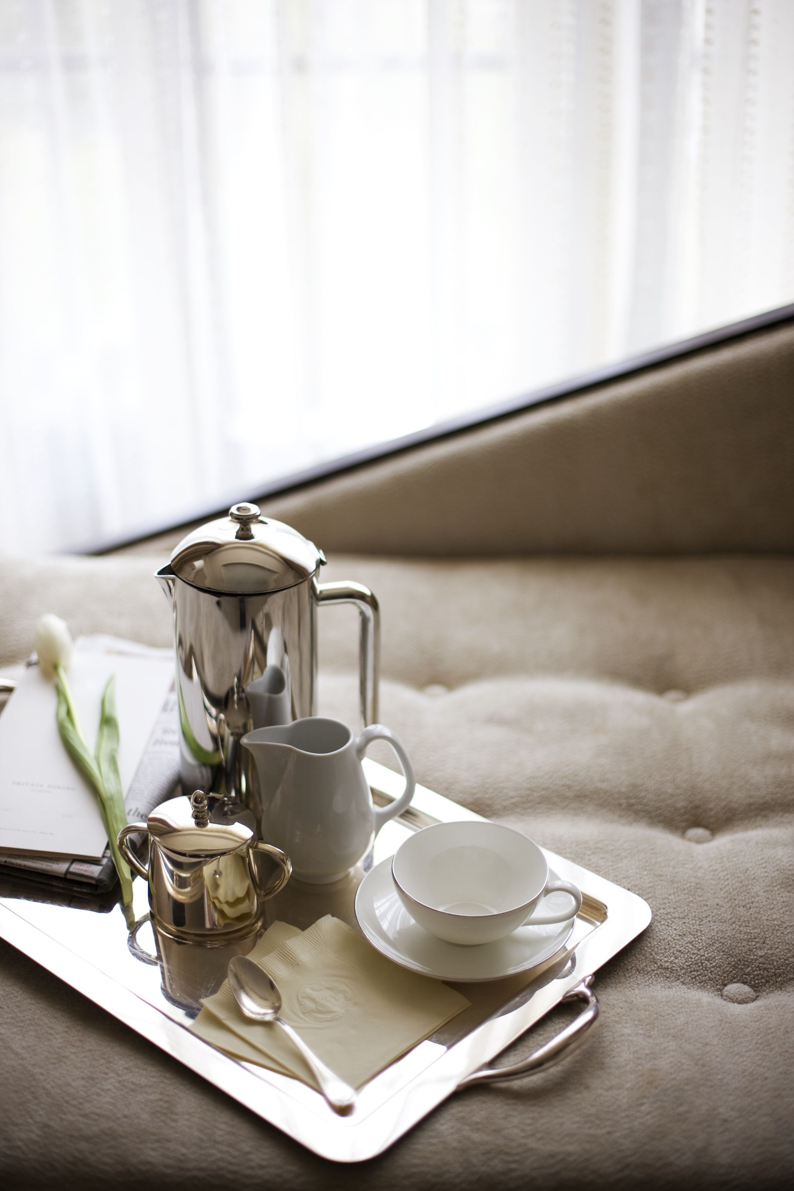 A tray with a silver coffee pot, a white cup, and a saucer on a beige sofa.