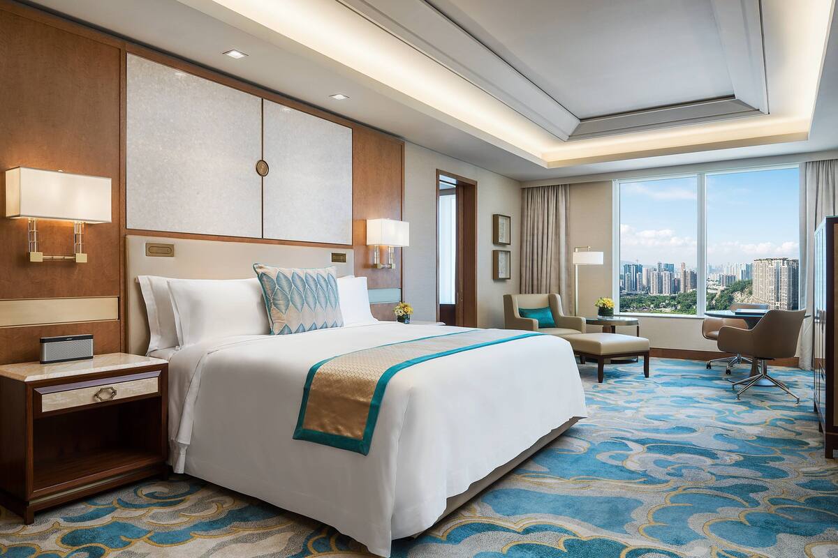 A hotel room with a large bed, a desk, a chair, and a view of the city.
