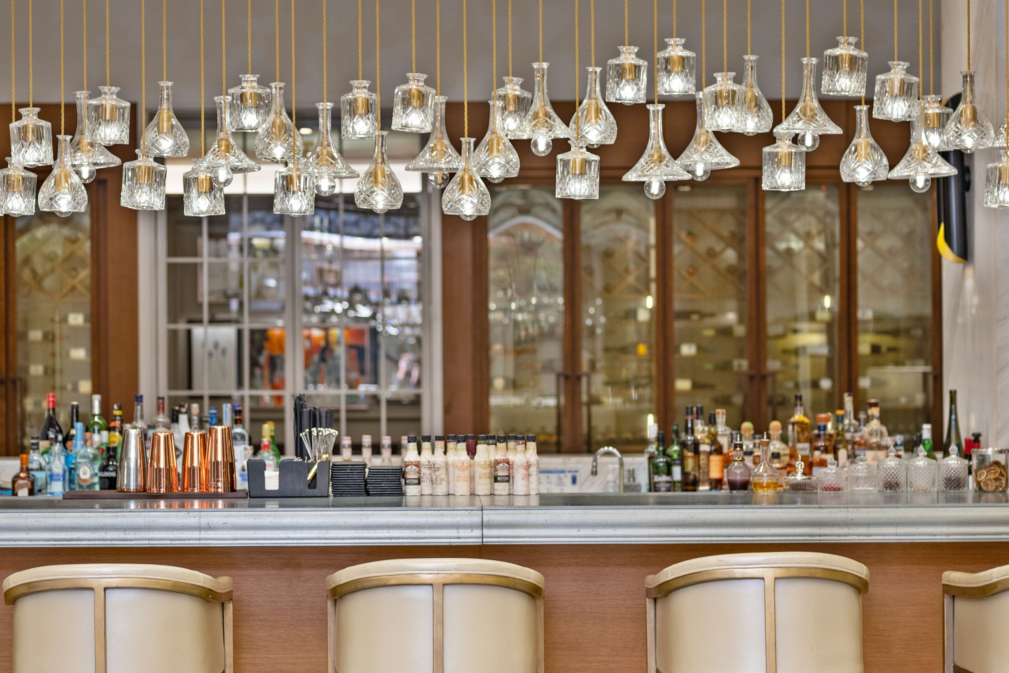 Un espace bar agrémenté de plusieurs luminaires suspendus en verre, ainsi que d’une variété de bouteilles et de verres disposés sur le comptoir.