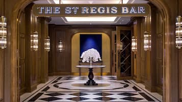 Eine Lobby mit einem Schachbrettmuster-Boden, einem Tisch mit Blumen in einer Vase und einem Schild mit der Aufschrift 'The St Regis Bar'.