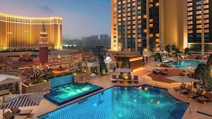 Zona de piscina de hotel con una piscina grande, tumbonas y vistas del horizonte urbano.