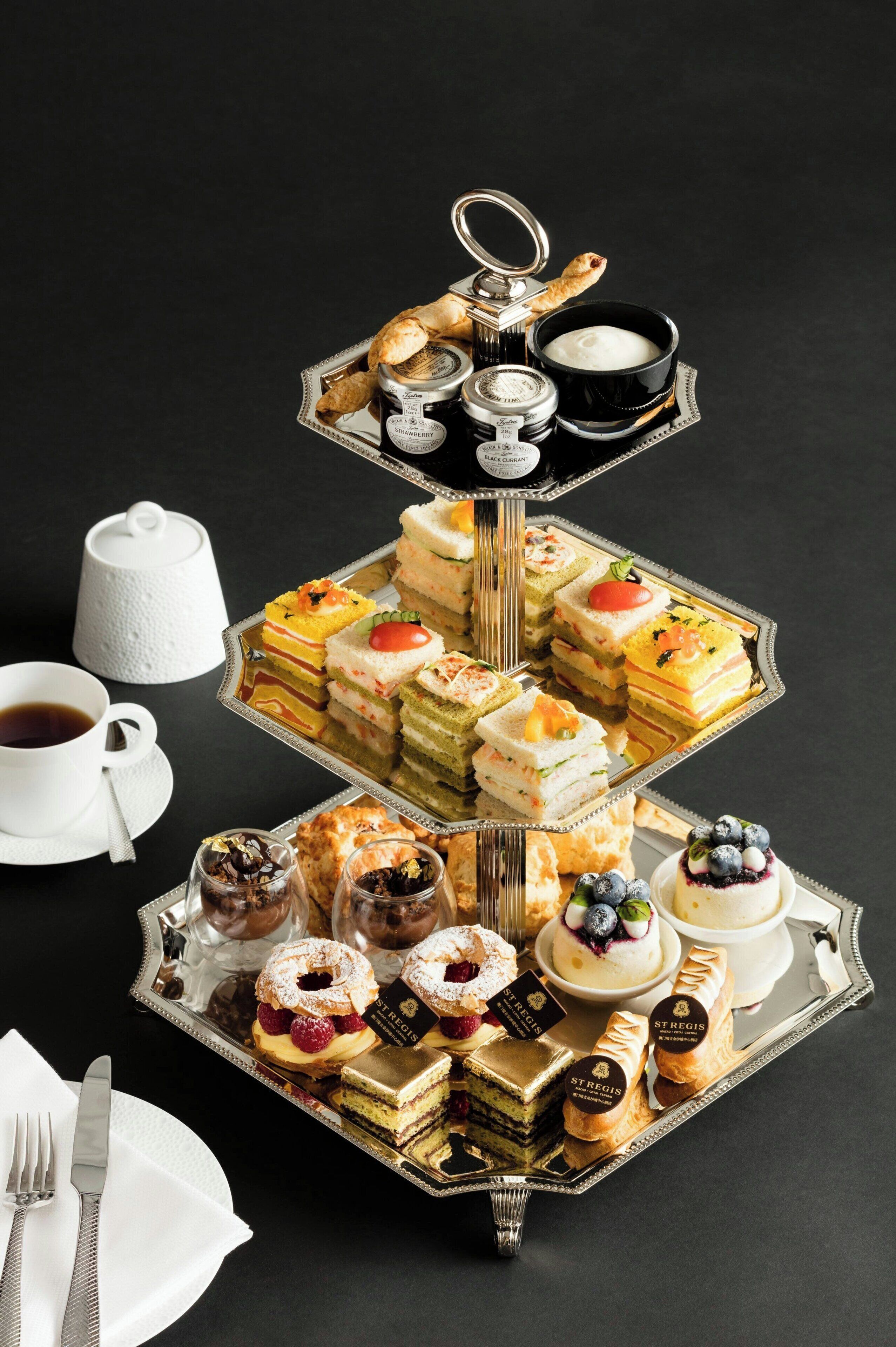 Una bandeja escalonada con diversos pasteles y tortas, una tetera y una taza de té.