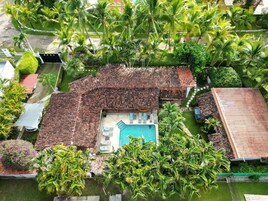 An aerial view of a house with a swimming pool, surrounded by palm trees and a tiled roof.