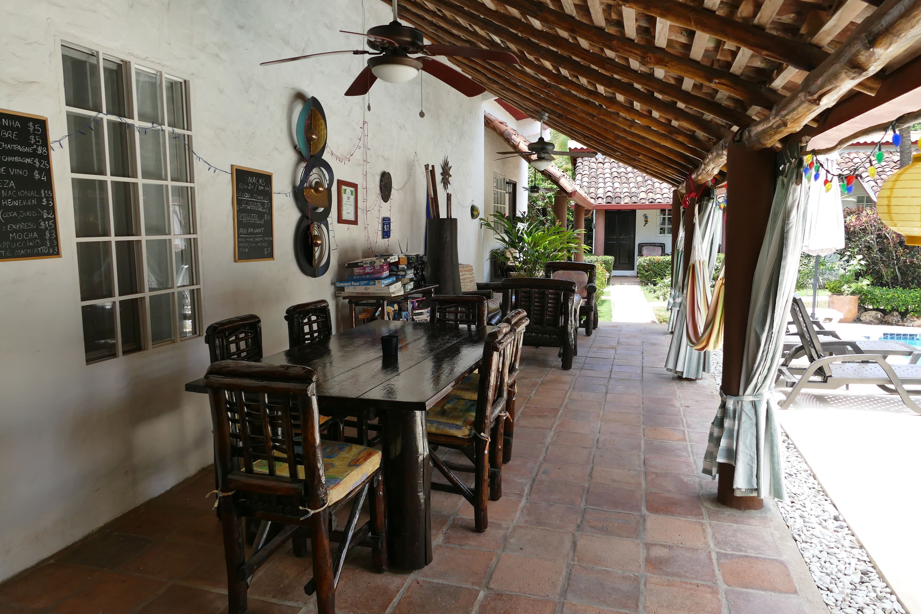 A covered patio with a wooden table and chairs, surrounded by white walls with various signs and decorations.