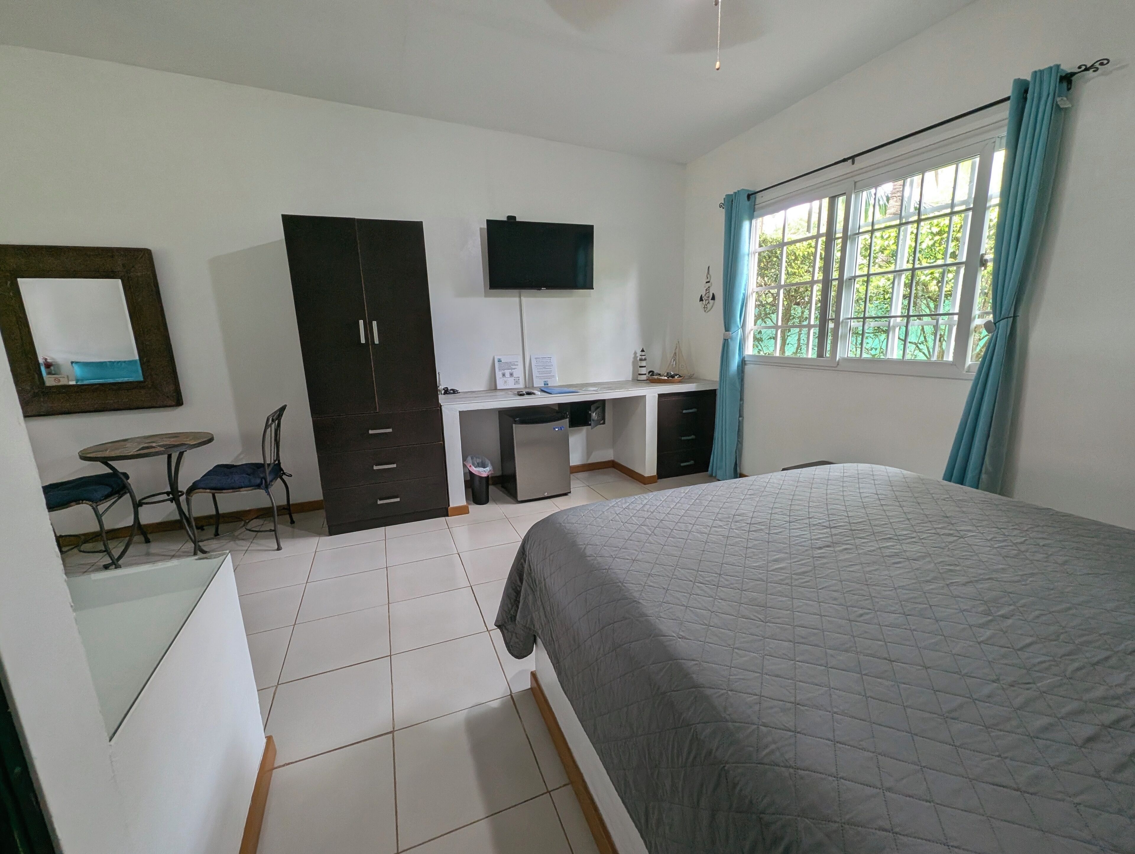 Un dormitorio con una cama, un escritorio con silla, un armario y un televisor en la pared.