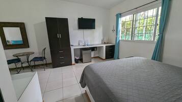 Un dormitorio con una cama, un escritorio con silla, un armario y un televisor en la pared.