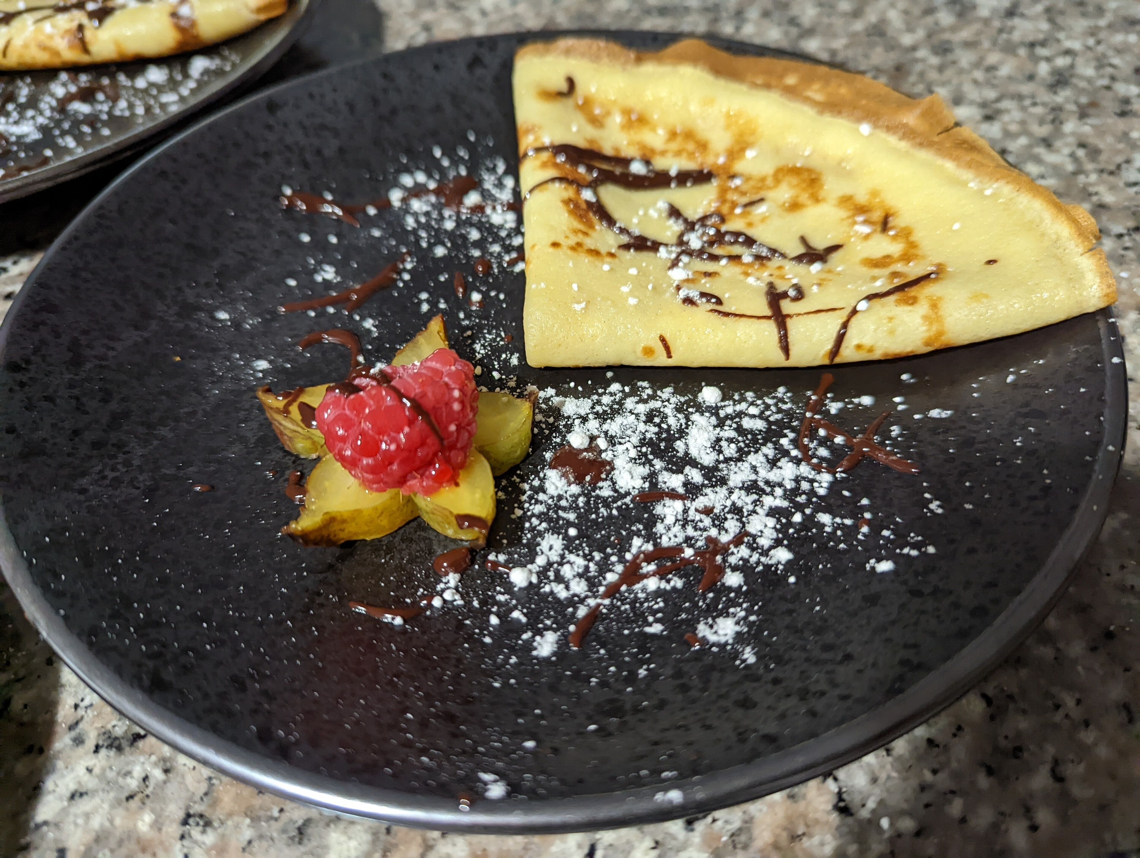 A plate with a crepe, raspberries, chocolate drizzle, and powdered sugar.