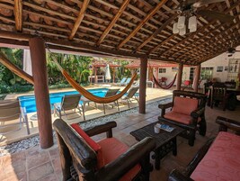 A covered outdoor area with a pool, hammocks, and wooden furniture.