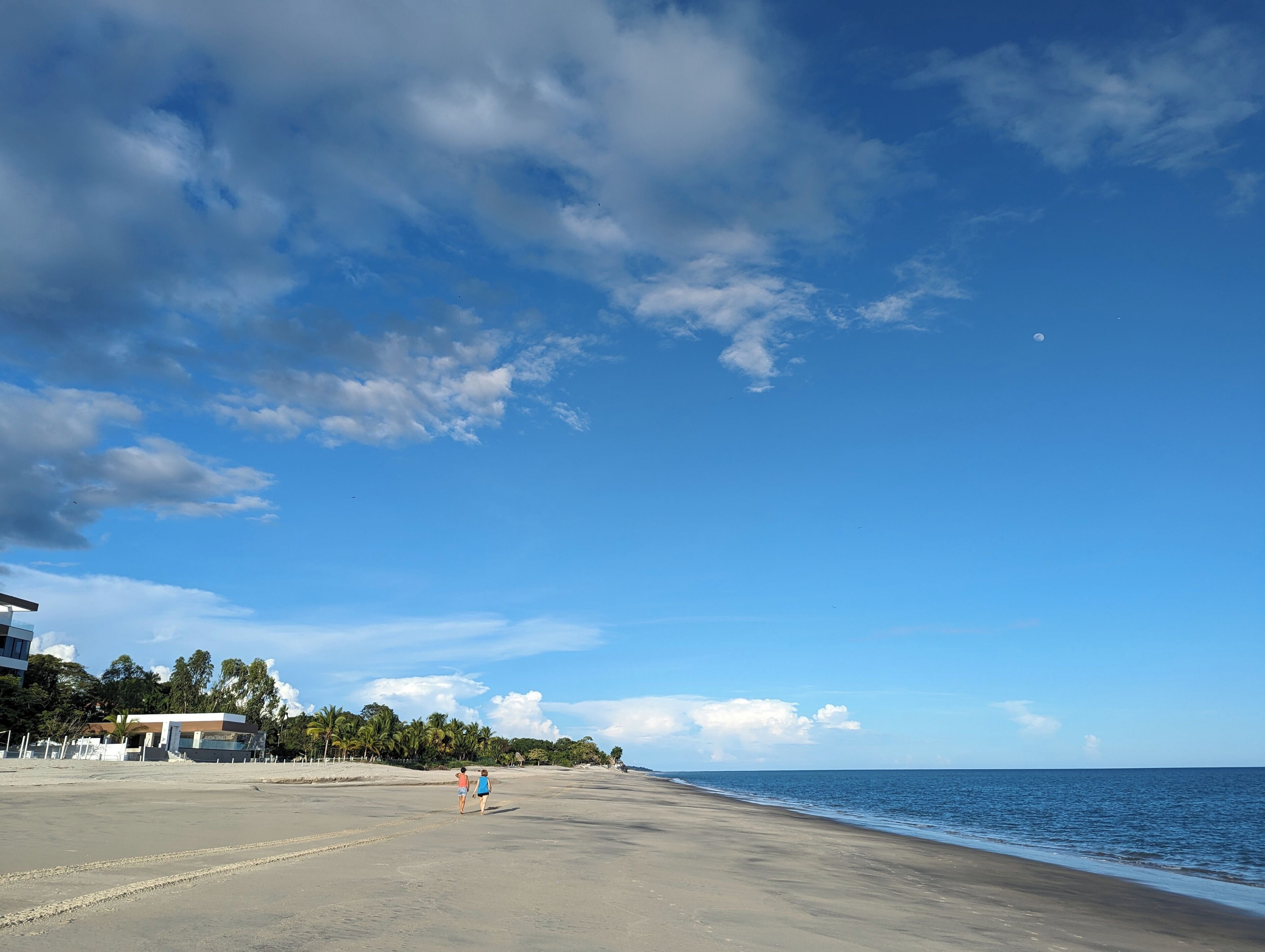A wide beach with a clear sky and a few clouds.