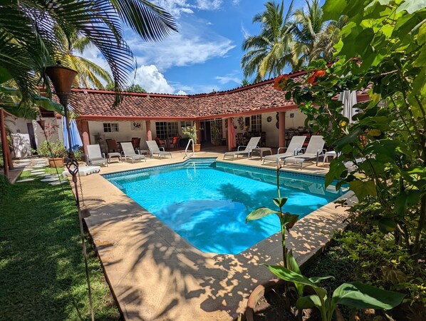 A swimming pool with lounge chairs, surrounded by greenery and a building with a tiled roof. - Villa Botero By Casa Mojito B&B (Rio Hato)