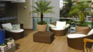 Un área de descanso al aire libre moderna con diversas opciones de asientos, incluyendo sofás y sillones, rodeada de plantas en macetas.