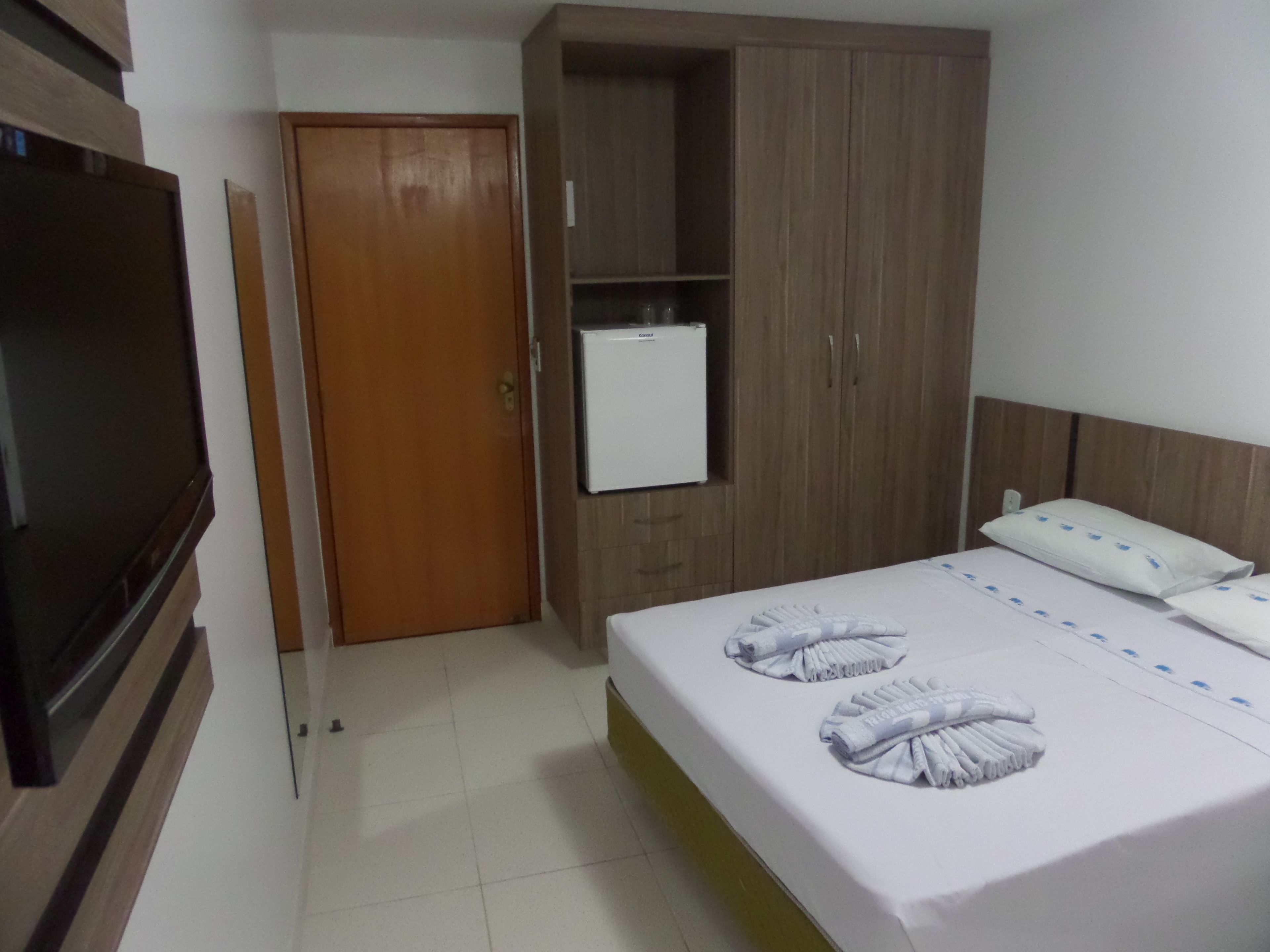 A hotel room with a bed, a TV, a wardrobe, and a mini-fridge.