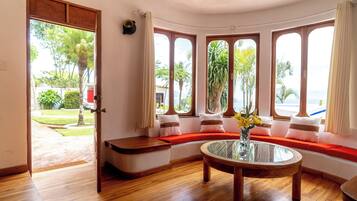 A room with a curved wooden bench, a glass coffee table, and a view of the outdoors through large windows.