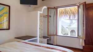 Une chambre à coucher avec un lit, un téléviseur fixé au mur, une fenêtre donnant sur les montagnes et une porte en bois.